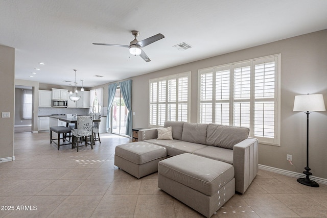 living room featuring light tile patterned flooring, visible vents, baseboards, and a ceiling fan