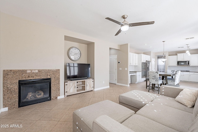 living room featuring visible vents, a ceiling fan, a fireplace, light tile patterned floors, and baseboards