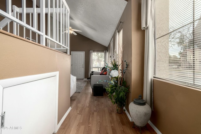 corridor featuring wood-type flooring, lofted ceiling, and a textured ceiling