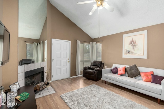 living room featuring ceiling fan, lofted ceiling, wood-type flooring, and a tiled fireplace