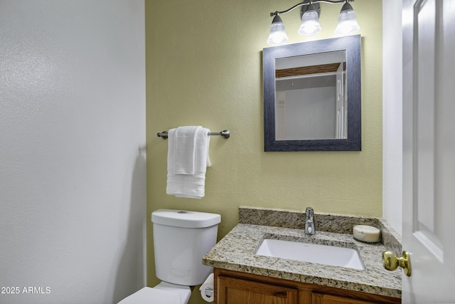 half bath with toilet, vanity, and a textured wall