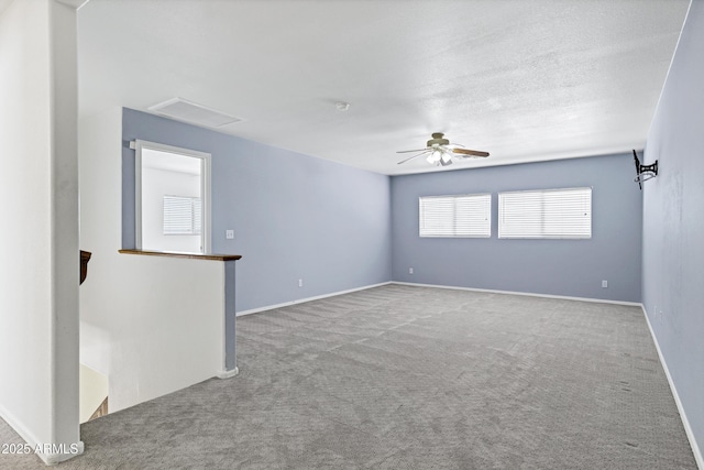 carpeted empty room featuring a textured ceiling, attic access, baseboards, and ceiling fan