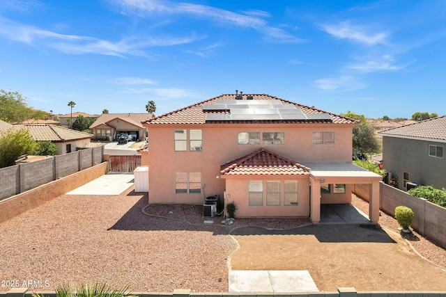 rear view of property with a tiled roof, a fenced backyard, roof mounted solar panels, and stucco siding