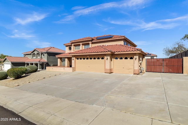 mediterranean / spanish home featuring solar panels, stucco siding, a garage, driveway, and a gate