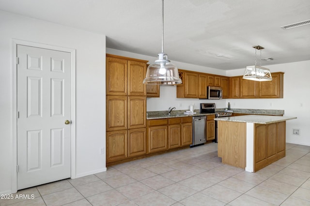 kitchen with a sink, appliances with stainless steel finishes, decorative light fixtures, brown cabinets, and a center island