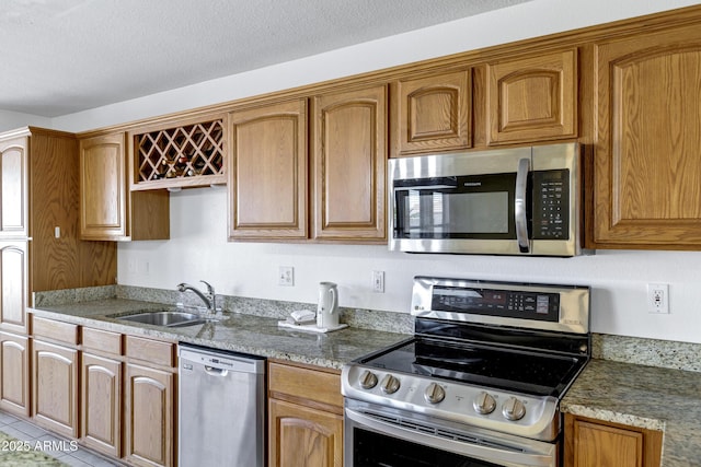 kitchen featuring a sink, a textured ceiling, stainless steel appliances, brown cabinetry, and light stone countertops