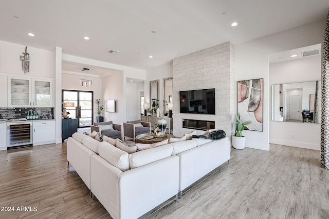 living room featuring wine cooler, a brick fireplace, and light wood-type flooring