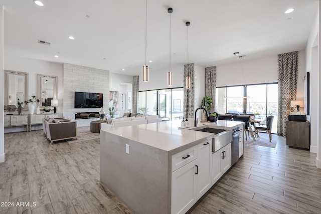 kitchen with pendant lighting, sink, light hardwood / wood-style floors, white cabinets, and a center island with sink