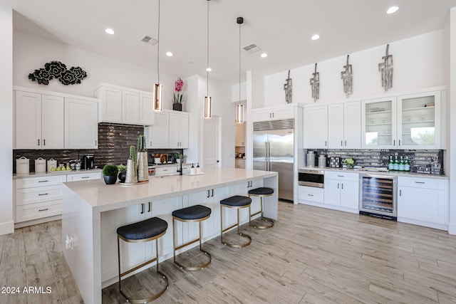 kitchen featuring a kitchen bar, white cabinetry, hanging light fixtures, built in fridge, and beverage cooler