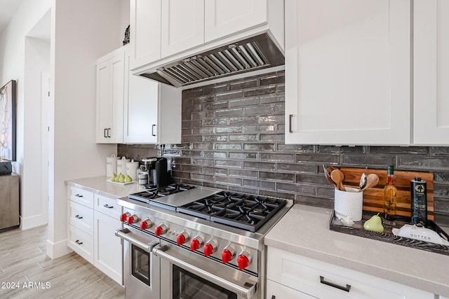 kitchen featuring backsplash, range with two ovens, custom range hood, white cabinets, and light wood-type flooring