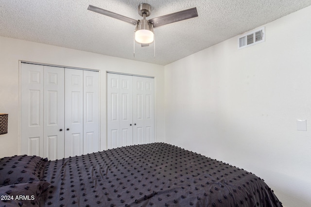 unfurnished bedroom featuring a textured ceiling, ceiling fan, and multiple closets