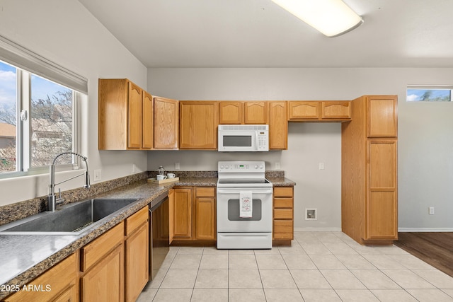 kitchen with light tile patterned floors, dark countertops, a sink, white appliances, and baseboards