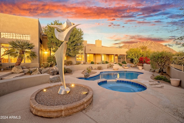 pool at dusk with an in ground hot tub and a patio