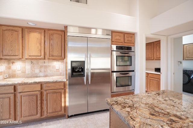 kitchen featuring light stone counters, decorative backsplash, washer and clothes dryer, light tile patterned flooring, and appliances with stainless steel finishes