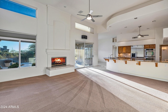 unfurnished living room featuring a large fireplace, sink, a towering ceiling, and light carpet