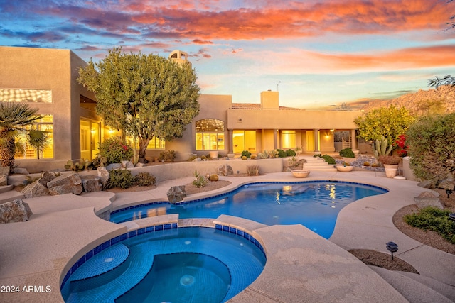 pool at dusk featuring an in ground hot tub and a patio