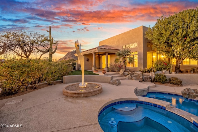 pool at dusk featuring an in ground hot tub and a patio