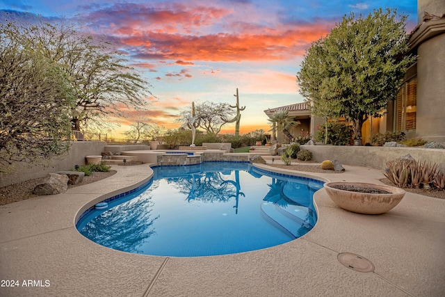 pool at dusk with a patio area and an in ground hot tub