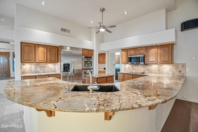 kitchen featuring a kitchen breakfast bar, decorative backsplash, a towering ceiling, and appliances with stainless steel finishes