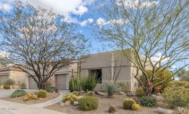 pueblo revival-style home with stucco siding, a garage, and driveway