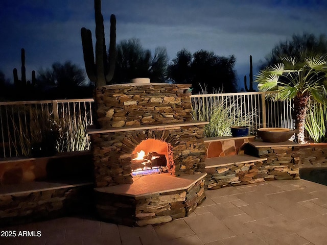 patio at night with an outdoor stone fireplace and fence