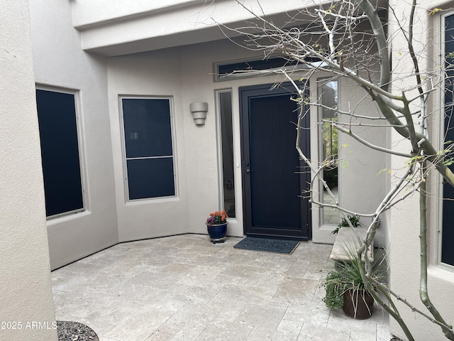 view of exterior entry with stucco siding and a patio