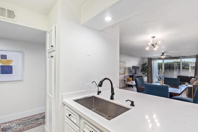 kitchen with white cabinets, ceiling fan with notable chandelier, light stone countertops, and sink