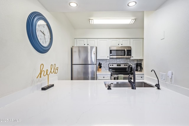 kitchen featuring decorative backsplash, appliances with stainless steel finishes, light stone counters, sink, and white cabinetry