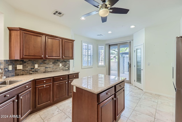 kitchen featuring stainless steel fridge, ceiling fan, backsplash, light stone countertops, and a center island