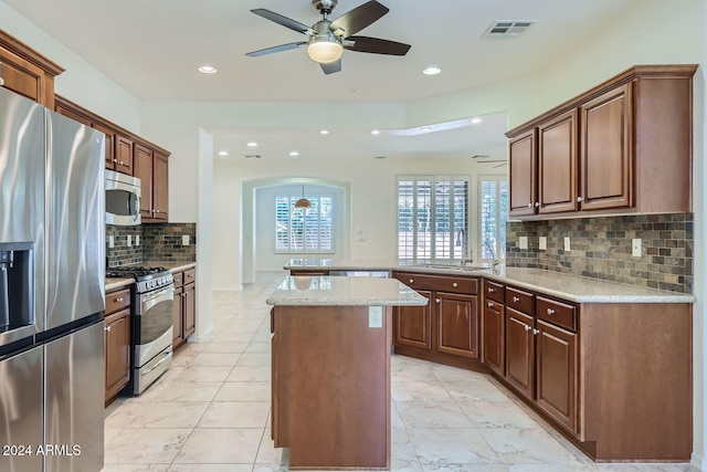 kitchen featuring appliances with stainless steel finishes, tasteful backsplash, ceiling fan, and a kitchen island