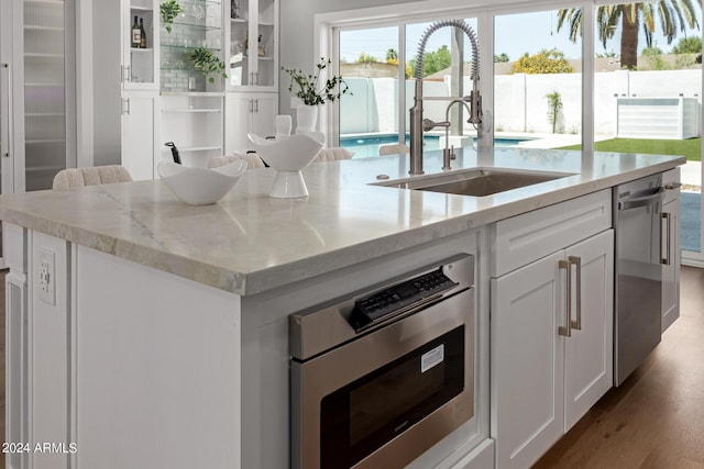 kitchen with a center island with sink, sink, light stone countertops, appliances with stainless steel finishes, and white cabinetry