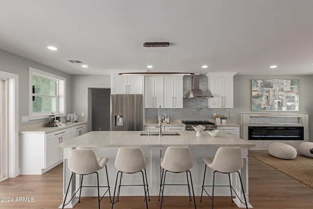 kitchen featuring white cabinetry, stainless steel fridge with ice dispenser, pendant lighting, and wall chimney range hood