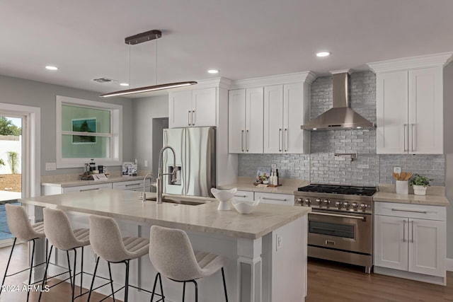 kitchen featuring white cabinetry, an island with sink, stainless steel appliances, and wall chimney range hood