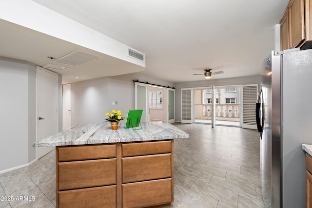 kitchen featuring stainless steel fridge, ceiling fan, a center island, light stone countertops, and a barn door