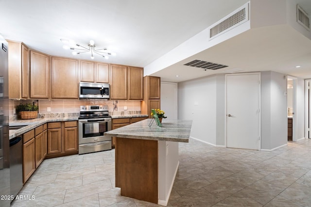 kitchen with tasteful backsplash, stainless steel appliances, light stone countertops, and a kitchen island