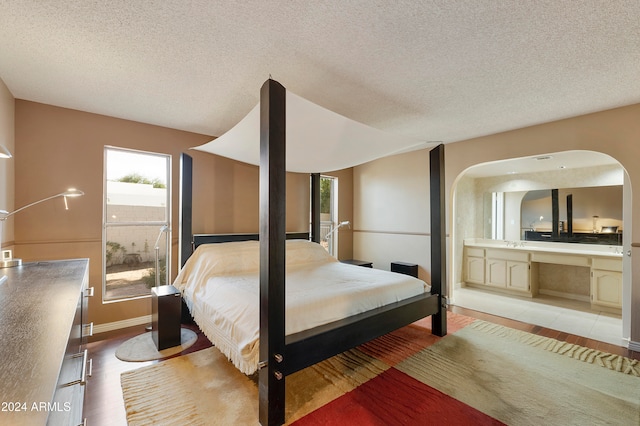 bedroom featuring connected bathroom, a textured ceiling, sink, and light wood-type flooring