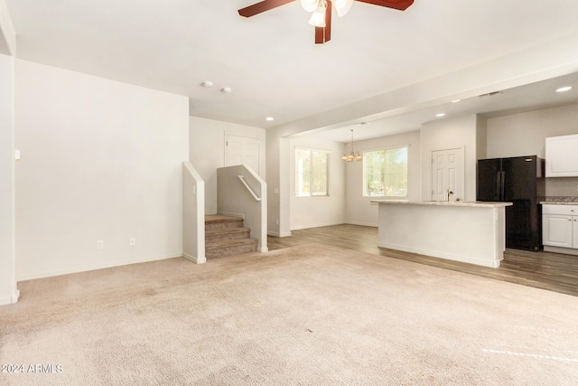 unfurnished living room featuring light colored carpet and ceiling fan with notable chandelier