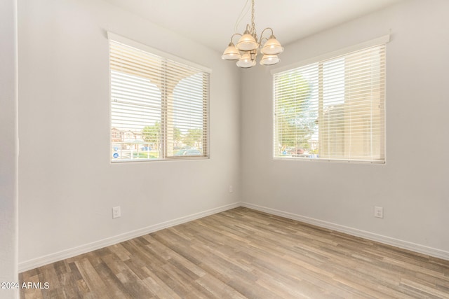 unfurnished room with a wealth of natural light, wood-type flooring, and an inviting chandelier