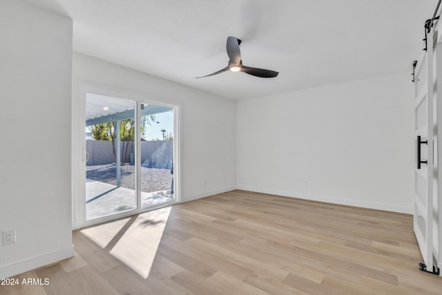 empty room featuring a barn door, light hardwood / wood-style floors, and ceiling fan