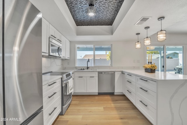 kitchen featuring appliances with stainless steel finishes, light wood-type flooring, sink, pendant lighting, and white cabinets