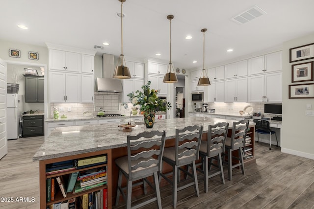 kitchen featuring light stone counters, a spacious island, wall chimney range hood, and white cabinetry