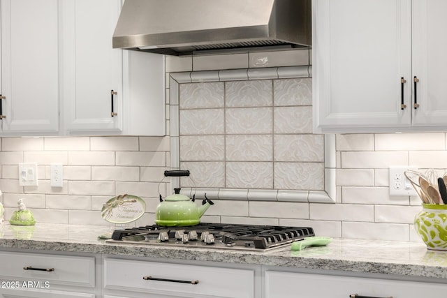 kitchen with backsplash, wall chimney range hood, and white cabinetry