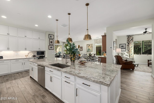 kitchen with light stone countertops, white cabinetry, sink, hanging light fixtures, and a center island with sink