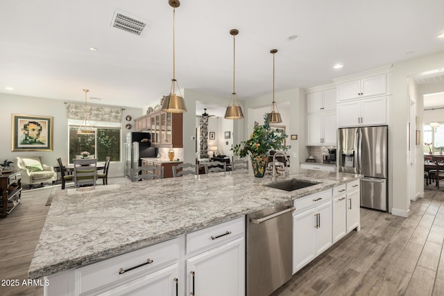 kitchen with a large island with sink, sink, stainless steel appliances, and white cabinetry