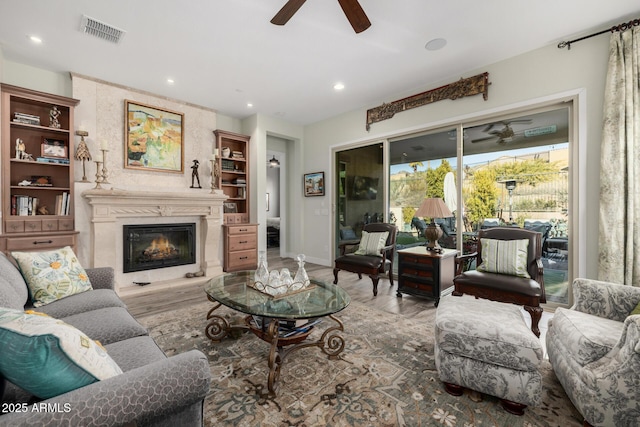 living room with ceiling fan, a large fireplace, and light hardwood / wood-style floors