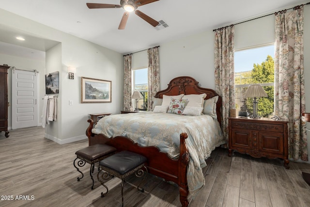 bedroom featuring ceiling fan, a barn door, multiple windows, and light hardwood / wood-style flooring