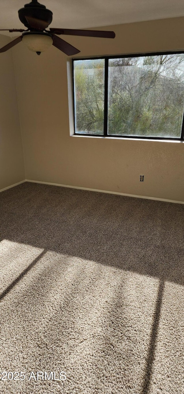 carpeted empty room featuring ceiling fan and baseboards