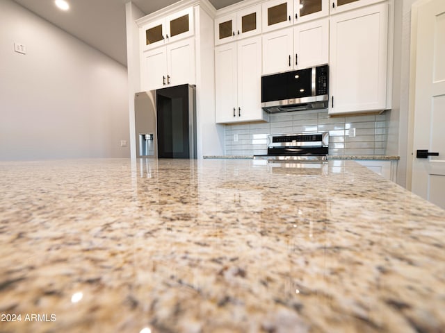 kitchen with tasteful backsplash, white cabinetry, light stone countertops, and appliances with stainless steel finishes