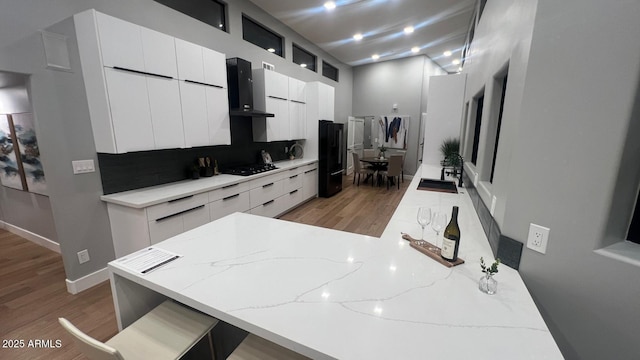 kitchen with wall chimney range hood, a breakfast bar area, black appliances, and white cabinets