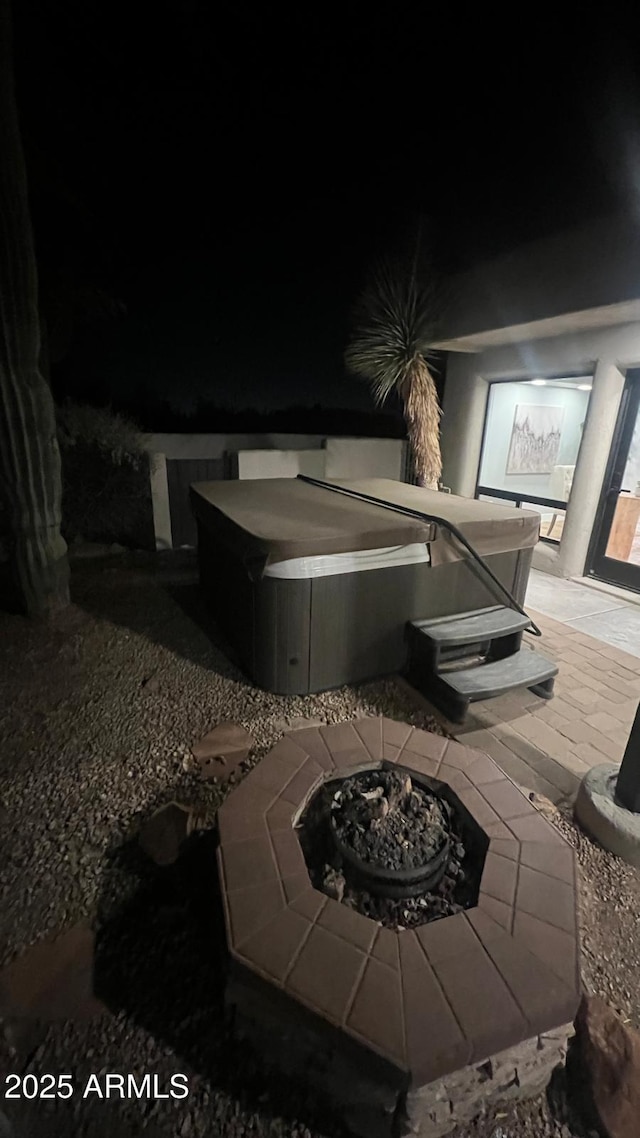 patio at night with a hot tub and an outdoor fire pit